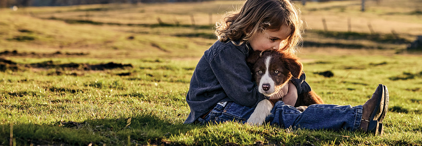 Child hugging dog in grass