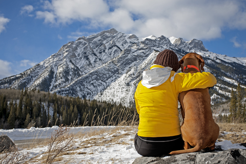 woman hiker and dog sitting looking at snow covered mountain