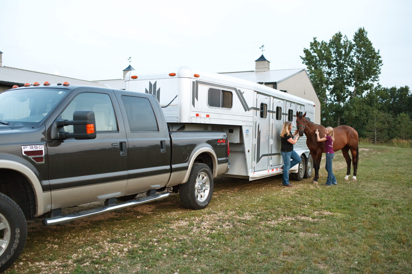 woman and daughter brushing horse near a trailer