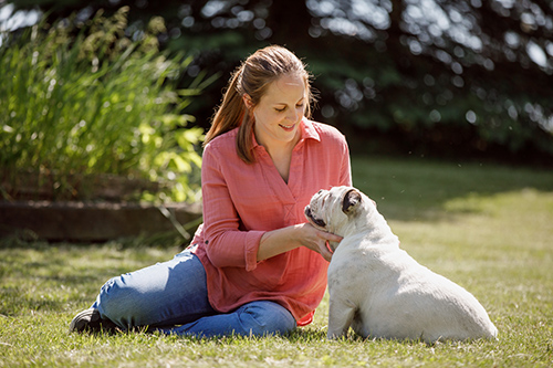 Woman sitting in grass with white bulldog